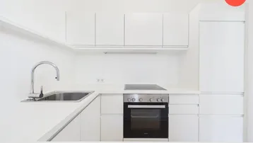 Moderne, weiße Einbauküche mit Induktionskochfeld, Backofen und integrierten Geräten.