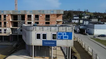 Baustelle eines modernen Neubaus mit sichtbaren Beton- und Ziegelstrukturen unter blauem Himmel.