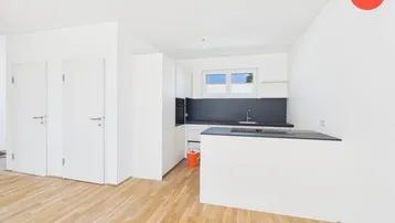 Moderne, offene Küche mit weißen Schränken, dunkler Arbeitsplatte und hellem Holzfußboden.