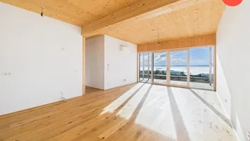 Heller, leerer Raum mit Holzbalkendecke, Parkettboden und großen Fenstern mit Weitblick.