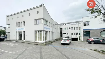 Modernes Geschäftsgebäude mit weißer Fassade, großen Fenstern und Parkplätzen im Vordergrund.