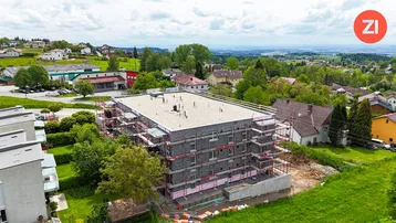 Luftaufnahme eines Neubaus mit Gerüst und bereits verputzter Fassade, umgeben von grüner Landschaft.