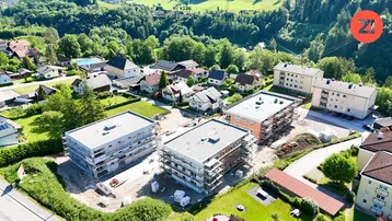 Luftaufnahme einer Wohnsiedlung mit Neubauten im Bau und grüner Umgebung, umgeben von Hügeln.