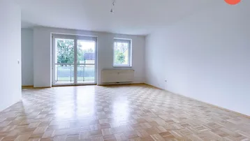 Helles, leeres Wohnzimmer mit Parkettboden und Zugang zu einem kleinen Balkon.