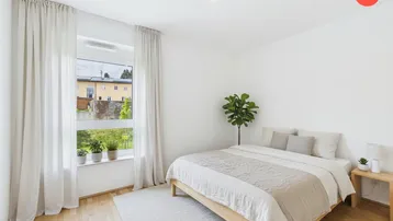 Helles Schlafzimmer mit Holzbett, Parkettboden und großem Fenster mit Blick ins Grüne.