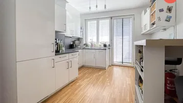 Helle Küche mit weißen Hochglanzfronten, Holzboden und Zugang zum Balkon.