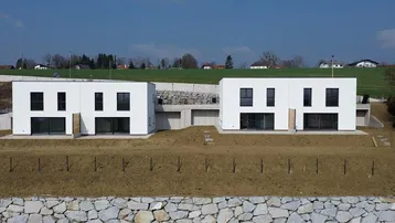Zwei moderne, weiße Neubauhäuser mit großen Fenstern in ländlicher Umgebung.