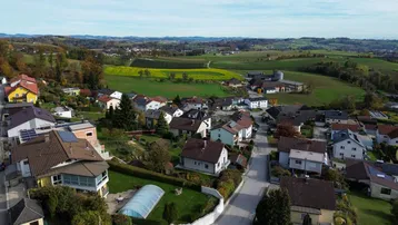 Weitläufige Luftaufnahme der Wohnsiedlung eingebettet in die grüne, hügelige Landschaft mit Feldern.