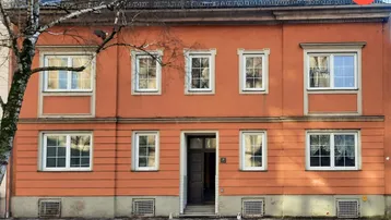 Klassische Fassade eines Wohnhauses in warmem Orangeton mit vielen Fenstern und Eingangstür.