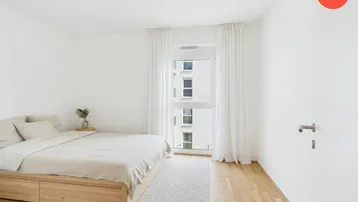 Helles Schlafzimmer mit Holzboden, weiß gestrichenen Wänden und Blick auf die Nachbargebäude.