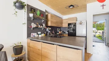 Moderne Küche mit Holzelementen, dunkler Arbeitsplatte, integrierten Geräten und Blick ins Grüne.