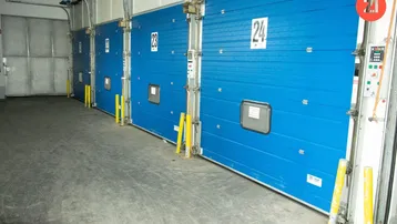 Reihe von blauen Laderampentoren in einer Lagerhalle mit Betonboden und industrieller Beleuchtung.