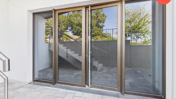 Eingangsbereich eines modernen Gebäudes mit großen Glasfronten und Außentreppe.