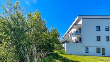 Modernes Mehrfamilienhaus mit weißer Fassade und Balkonen, umgeben von viel Grün.
