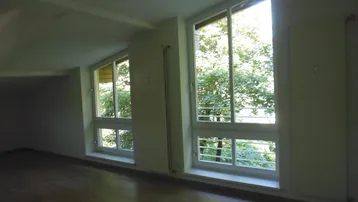 Helles Zimmer mit schrägen Fenstern, Holzboden und Blick ins Grüne.
