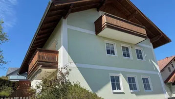 Gebäudeansicht mit hellgrüner Fassade, Holzbalkonen und Satteldach.