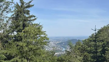 Panoramablick über eine Stadt und einen Fluss, umgeben von grünen Wäldern und Bergen.