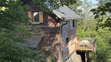 Charmantes Holzhaus in Hanglage mit seitlicher Terrasse und umgebendem Wald.