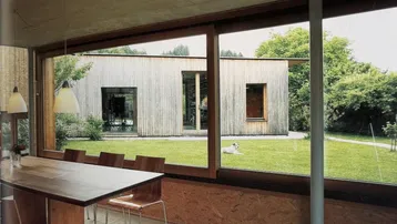 Moderner Essbereich mit Holztisch und großen Fenstern, die einen Blick auf den Garten bieten.