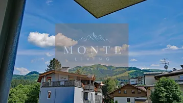 Panoramablick auf die umliegende Berglandschaft und grüne Hügel unter blauem Himmel.