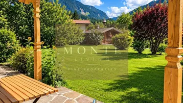 Gemütliche Terrasse mit Holztisch und Blick auf den gepflegten Garten und die Berge.