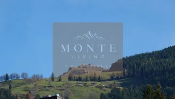 Malerische Berglandschaft mit einem Gebäude auf einem Hügel unter blauem Himmel.