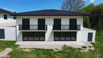 Neubau-Doppelhaushälfte mit moderner Architektur, Balkonen und kleiner Terrasse im Grünen.