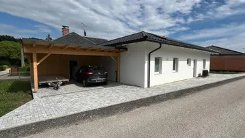 Modernes Einfamilienhaus mit Carport und gepflasterter Auffahrt unter bewölktem Himmel.
