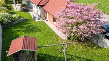 Luftaufnahme des Hauses mit blühendem Baum, großem Rasen und Kinderspielplatz im Garten.