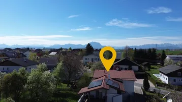 Luftaufnahme eines Hauses mit Solaranlage und weitem Blick auf die umliegende Landschaft und die Alpen.