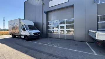 Modernes Industriegebäude mit großem Sektionaltor und einem Lieferwagen auf dem Parkplatz.
