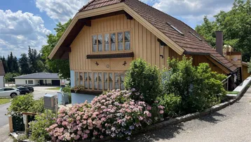 Traditionelles Holzhaus mit Satteldach und blauer Fassade, umgeben von blühenden Hortensien.