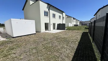Rückseite eines Neubaus mit kleiner Terrasse und Gartenbereich unter blauem Himmel.