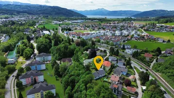 Panoramische Luftaufnahme einer Ortschaft mit See und Bergen im Hintergrund, die Lage markierend.