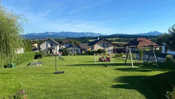 Großer Garten mit gepflegter Rasenfläche, Spielgeräten und weitem Blick auf die Berge.