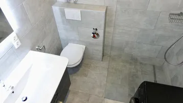 Modernes Badezimmer mit grauen Fliesen, WC, Waschbecken und Duschbereich, inklusive Waschmaschine.