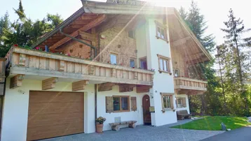 Traditionelles Holzhaus im alpinen Stil mit Garage und Balkonen, umgeben von viel Grün.