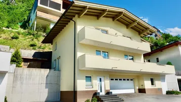 Mehrstöckiges Wohnhaus mit Balkonen und integrierter Garage am Hang gelegen.