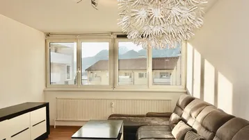 Gemütliches Wohnzimmer mit großem Fenster, Bergblick, bequemer Couch und auffälliger Deckenleuchte.