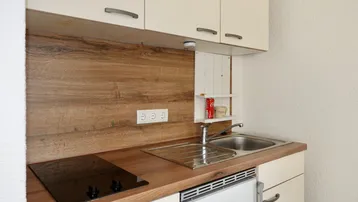 Kleine Küchenzeile mit Holz-Arbeitsplatte, Spüle, Induktionskochfeld und integriertem Kühlschrank.