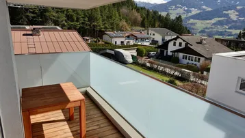Balkon mit Holzboden und Glasbrüstung, bietet einen weiten Blick auf die Berge und die Umgebung.