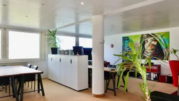 Geräumiges Großraumbüro mit modernen Möbeln, Pflanzen und farbenfroher Wandkunst.