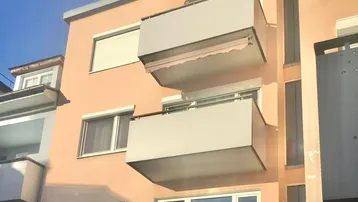 Fassade eines Wohngebäudes mit mehreren Balkonen und Rollläden an den Fenstern.