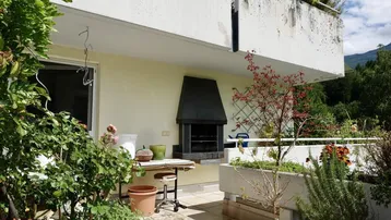 Geräumige Terrasse mit eingebautem Grill, vielen Pflanzen und Blick auf die umliegende Natur.