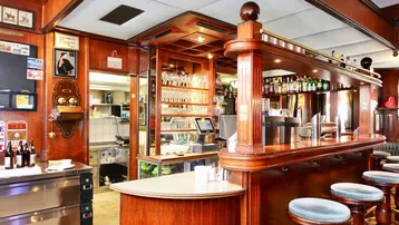 Eine traditionelle Bar mit dunklem Holz, Barhockern und einer gut bestückten Theke, die zum Verweilen einlädt.