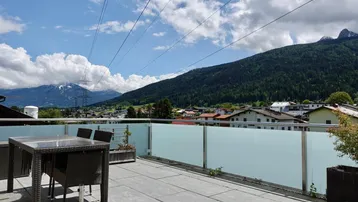 Sonnenterrasse mit Gartenmöbeln und weitem Panoramablick auf Berge und umliegendes Dorf.