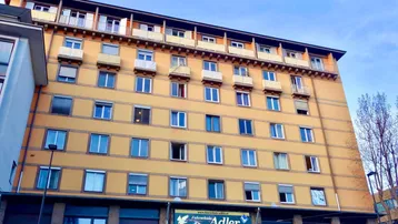 Mehrstöckiges Gebäude mit gelber Fassade, vielen Fenstern und kleinen Balkonen unter blauem Himmel.