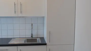 Moderne Küche mit weißen Schränken, dunkler Arbeitsplatte, Spüle und gefliestem Spritzschutz.