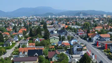 Weitläufige Ansicht einer Wohnsiedlung mit vielen Häusern und grünen Hügeln im Hintergrund.