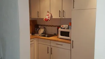 Kleine, funktionale Küche mit weißen Schränken, Holzarbeitsplatte und integrierter Spüle.